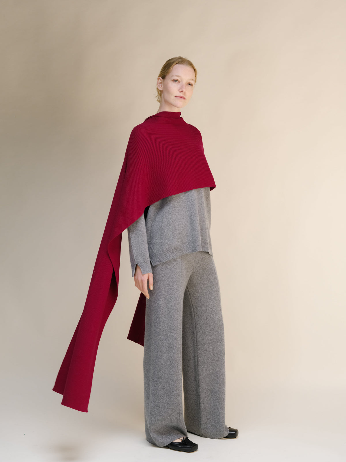 Person trägt einen breiten roten Kaschmirschal über einem grauen Outfit vor beigefarbenem Hintergrund