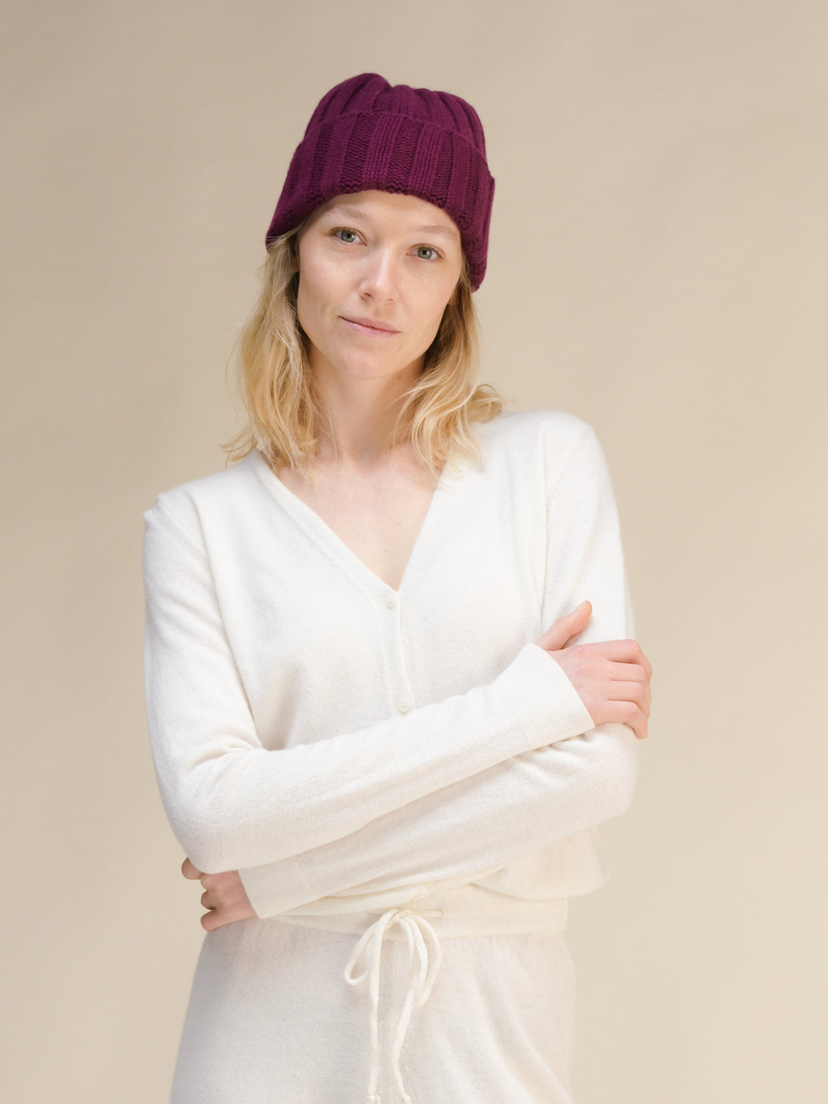 Woman wearing a white sweater and burgundy beanie against a beige background