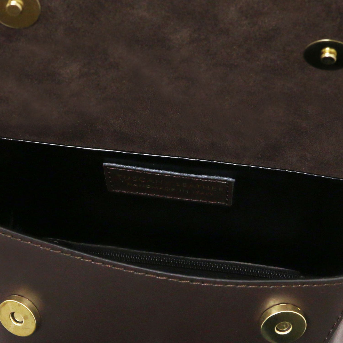 Close-up of a dark brown leather handbag interior showing a zippered pocket, a black interior lining, and brass-tone hardware.