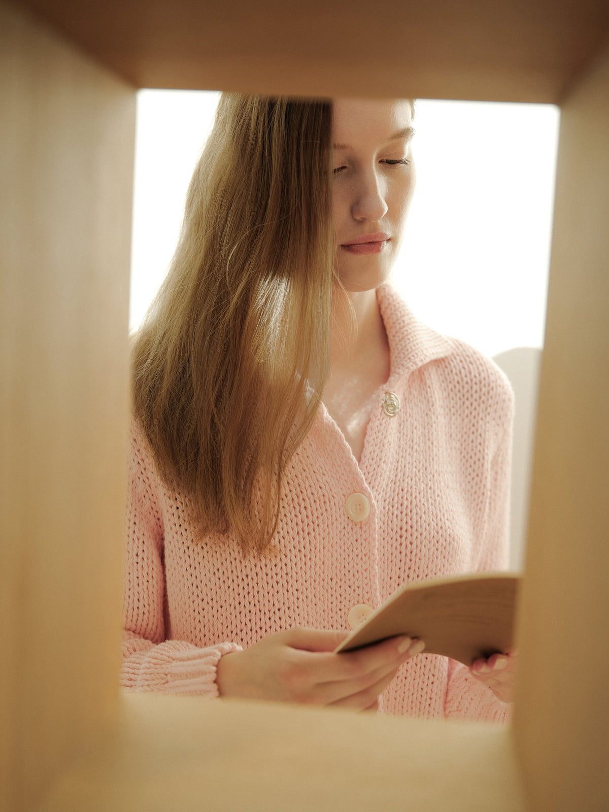 Vrouw in a pink knit cardigan with large white buttons holding a small notebook.