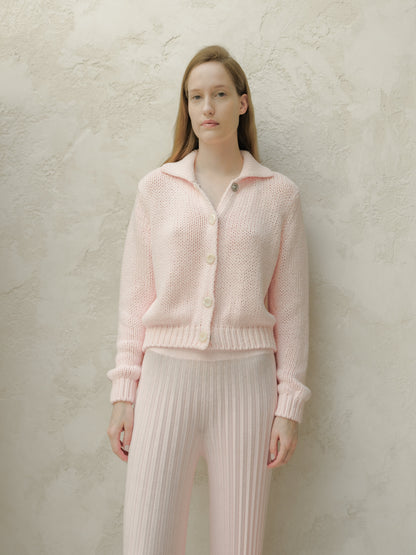 Front view of a model wearing a soft pink knitted cardigan with large white buttons against a textured beige wall