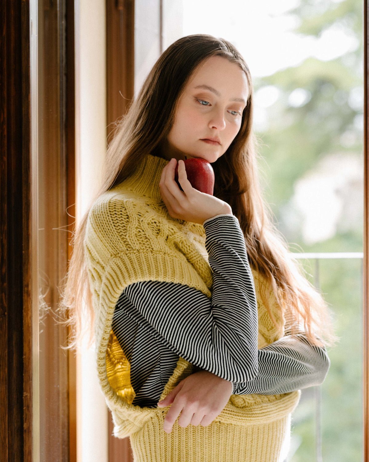 Modella con a crema cashmere mix maxi tunica a trecce over a striped top, holding a rosso apple near her face.