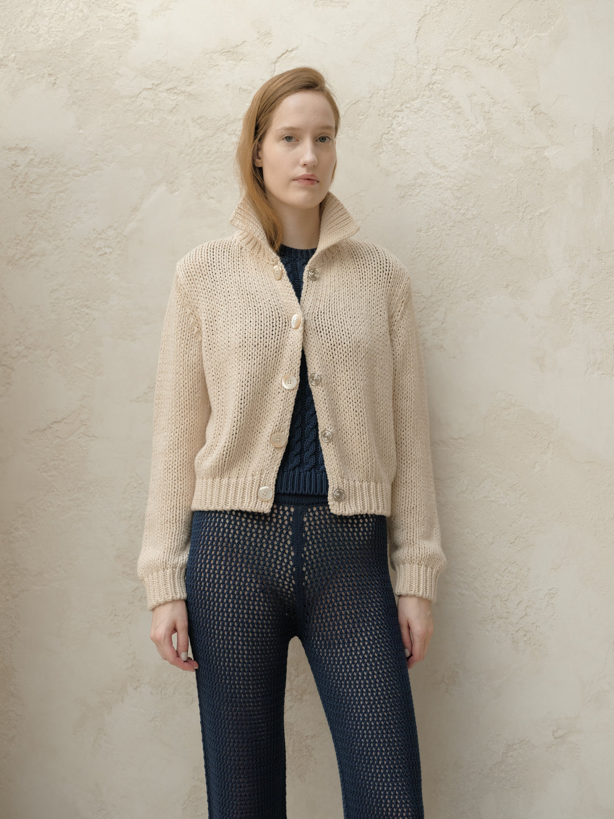 Beige chunky knit bomber jacket with large buttons and a high collar worn by model facing forward