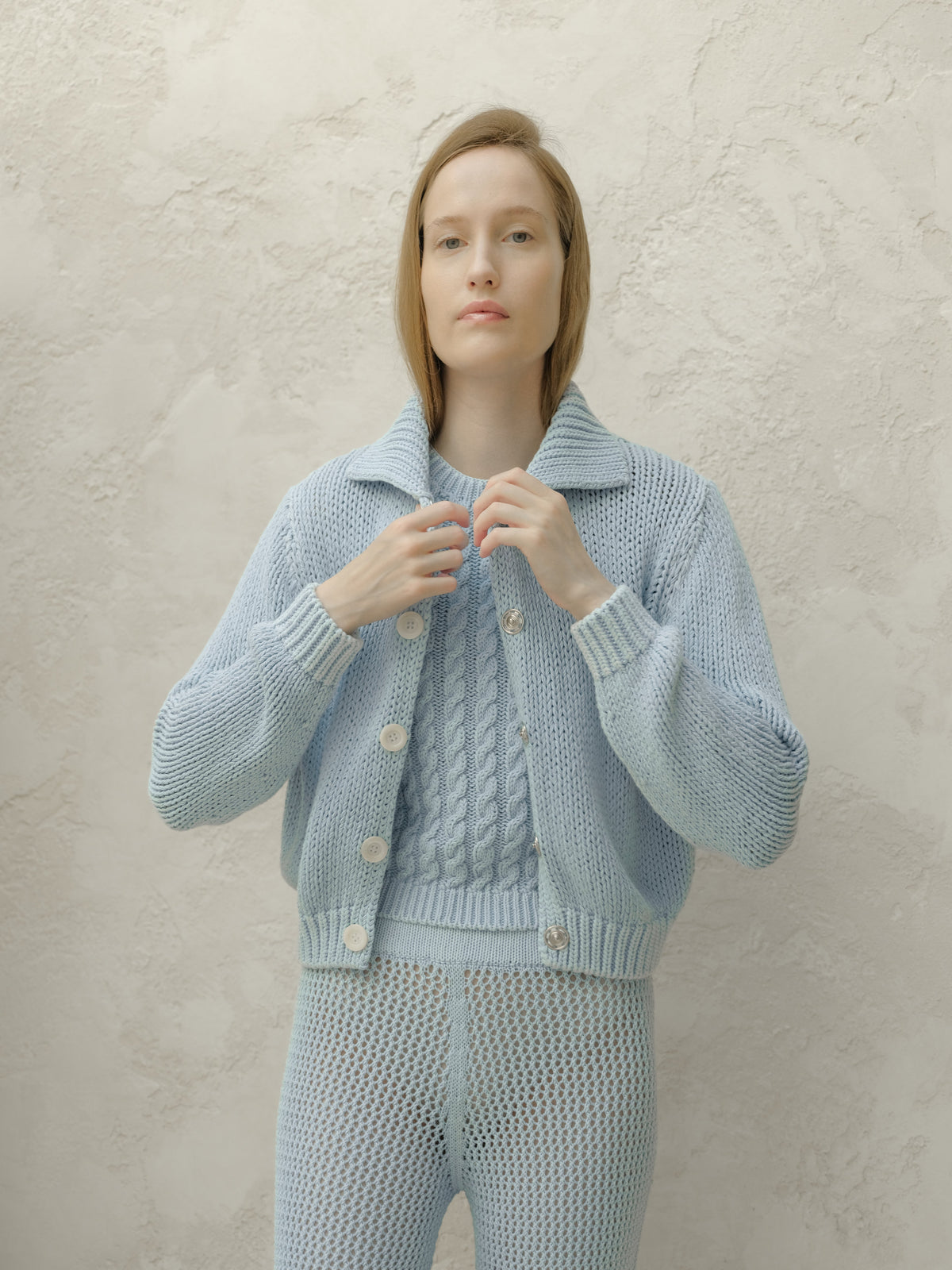 Front view of pale blue chunky knit bomber cardigan with large white buttons.