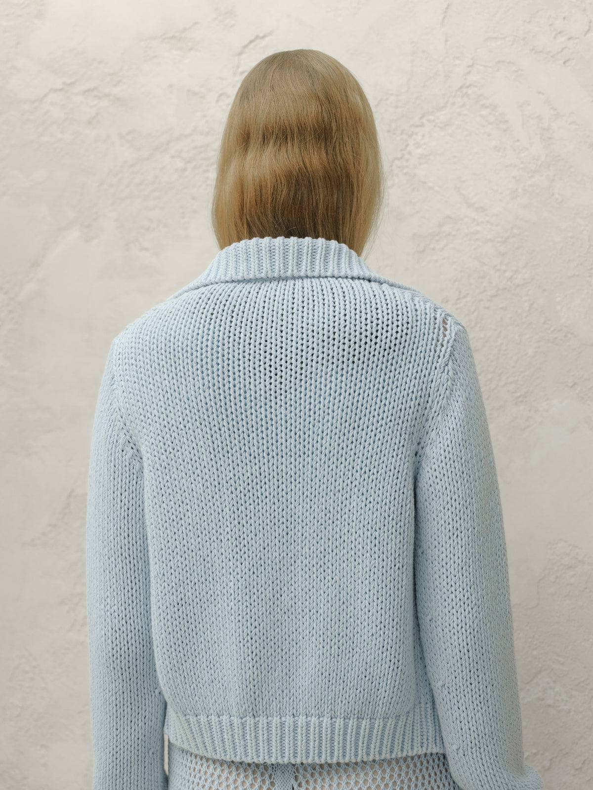 Back view of a model wearing a light blue chunky knit bomber jacket with a ribbed collar and hem.