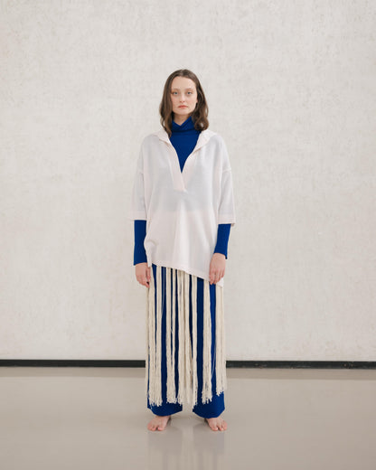 Model wears a pale cream Maxi polo en laine mérinos extrafine with a royal blue underlayer and a long fringe skirt.