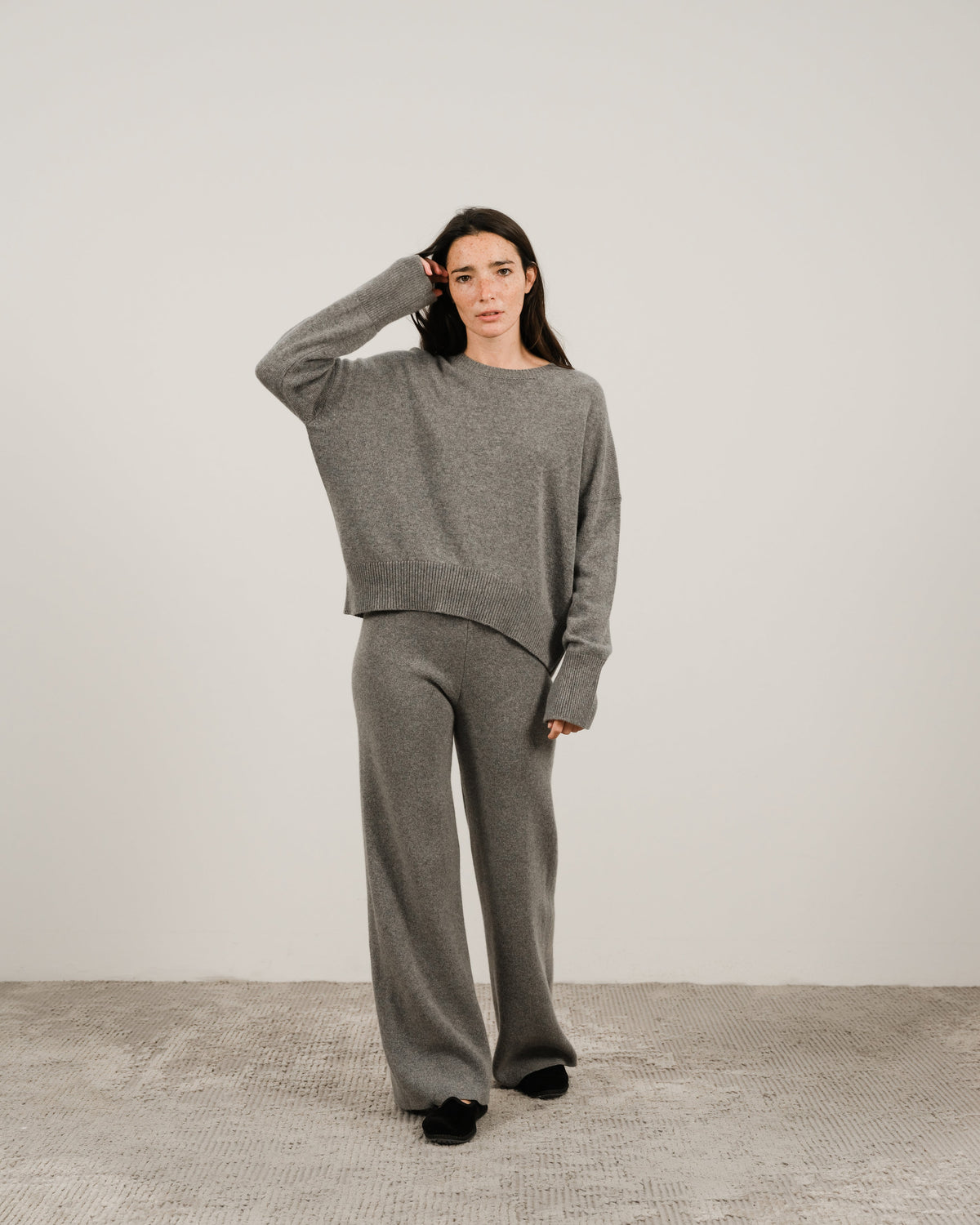 Modella con a grigio oversized cashmere mix maglione girocollo con pantaloni coordinati a gamba larga in a studio.