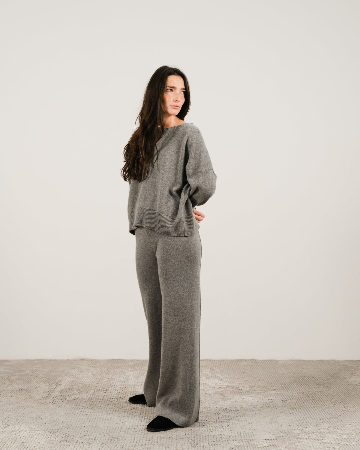 Donna con grigio cashmere mix maglione girocollo con pantaloni coordinati a gamba larga steing in a studio setting.