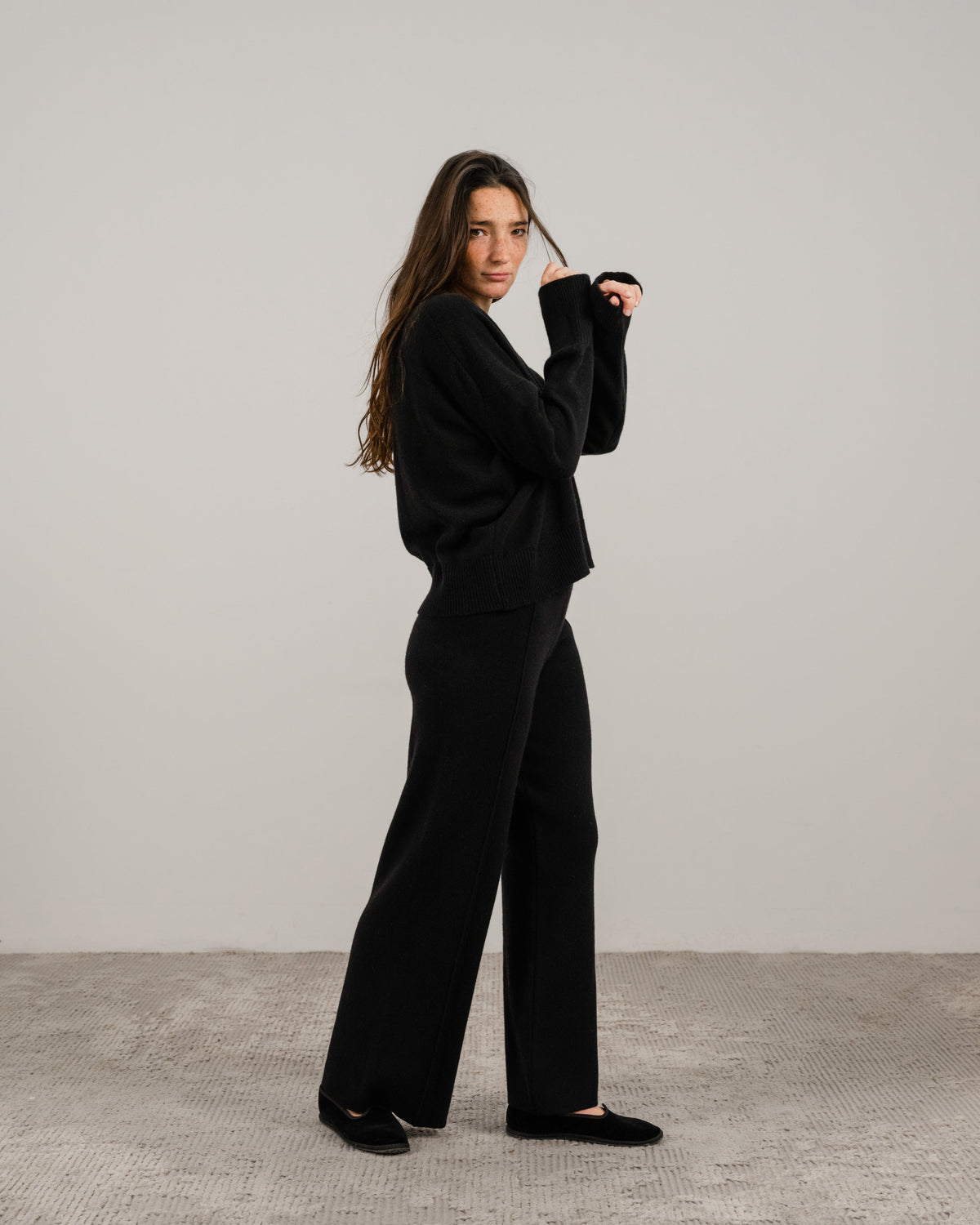 Full body vista laterale of a woman in a nero cashmere mix maglione girocollo con pantaloni a gamba larga