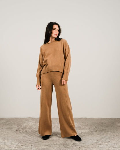 Front view of a woman in camel cashmere mix maglione girocollo e pantaloni coordinati a gamba larga in a neutral studio.