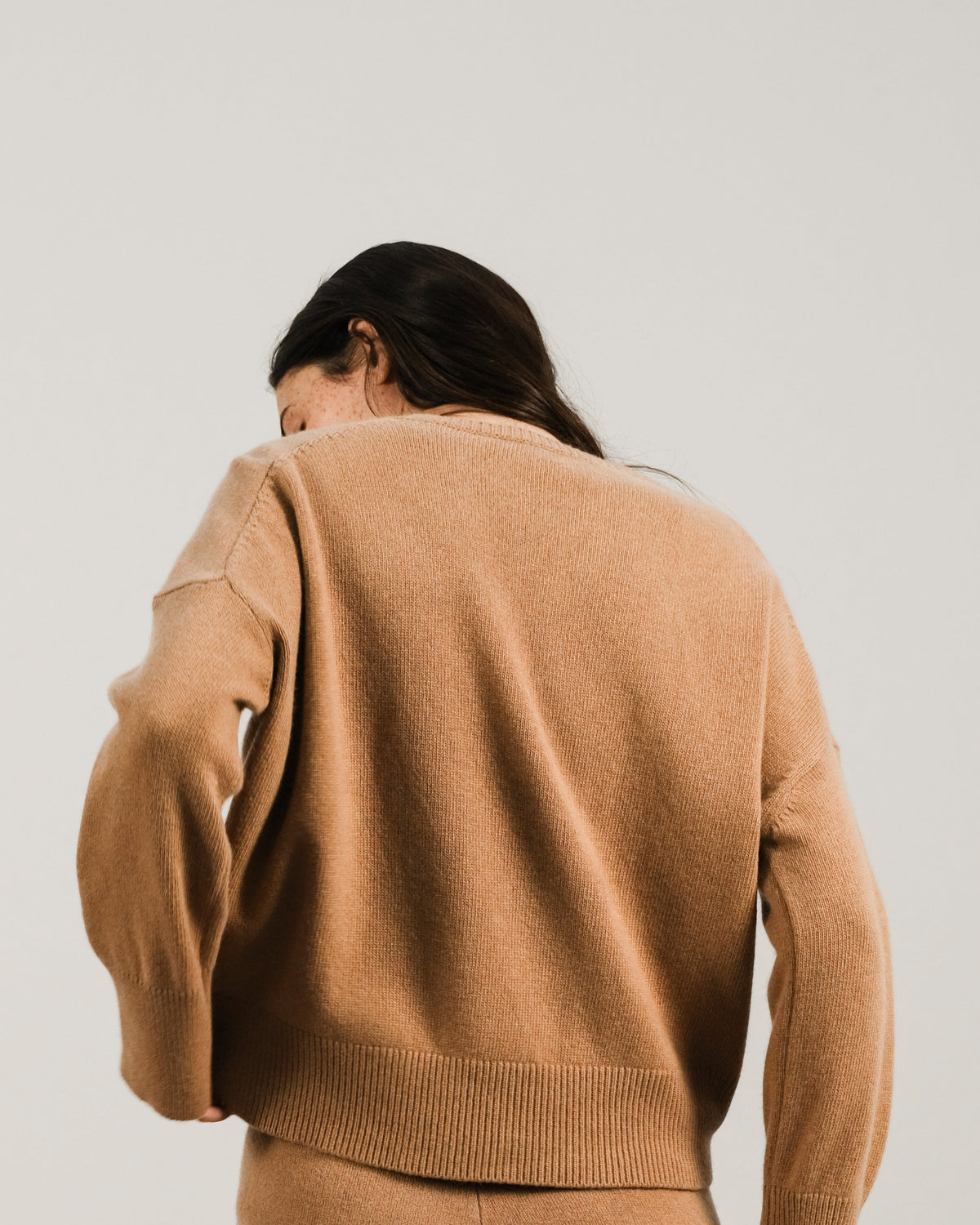 Back view of a woman in camel cashmere mix maglione girocollo e pantaloni coordinati.