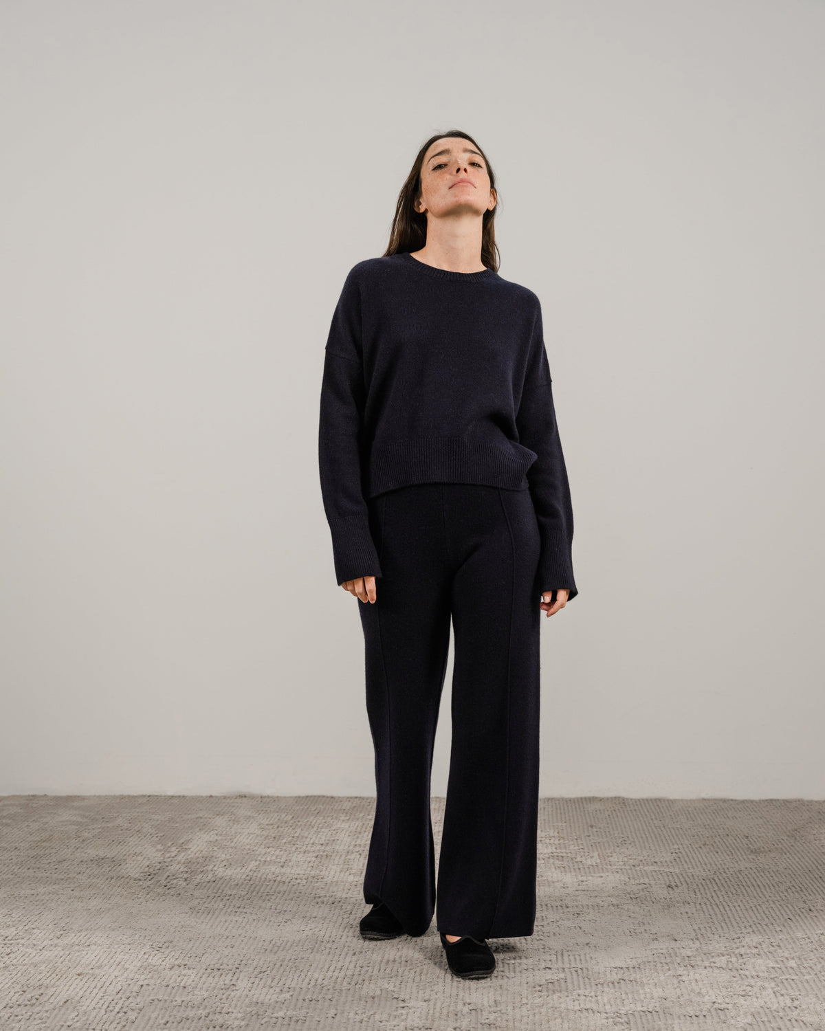 Modella con navy cashmere mix maglione girocollo e matching dark pants against a neutral backdrop.