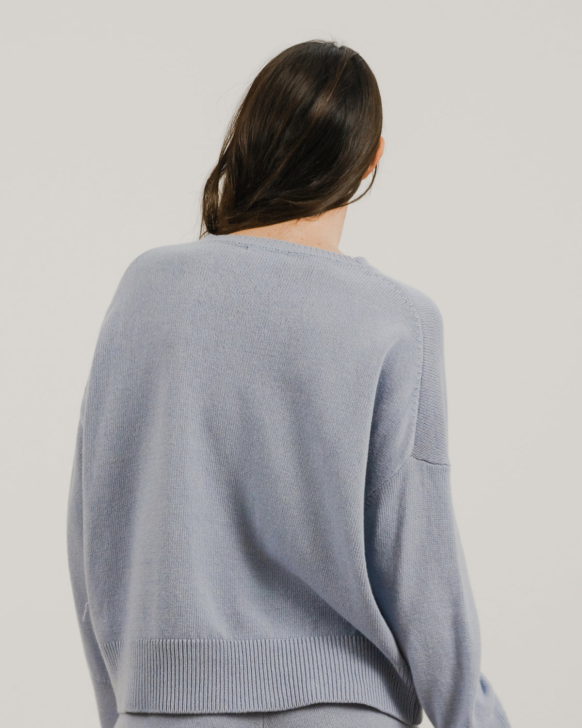 Back view of a loose light blu cashmere mix maglione girocollo on a model con a orlo a coste