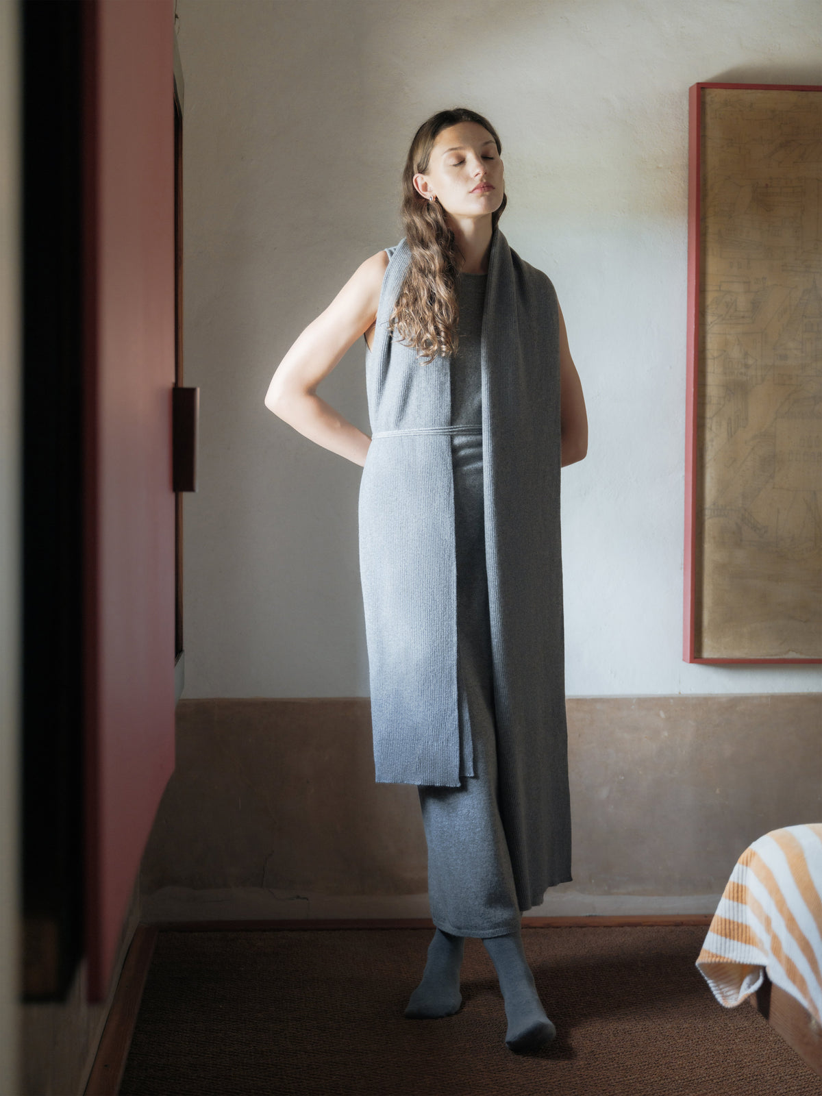 Frau trägt a long gray belted scarf over a dress in a room with a painting on the wall.