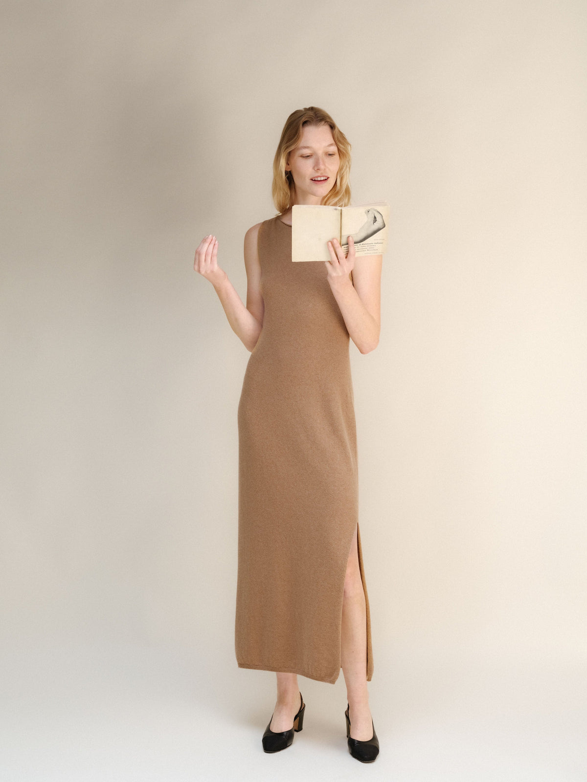 Full-length modelo con a taupe cashmere blend boat neck sleeveless dress and reading a book