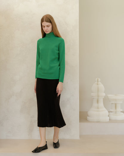 Modelo con verde intenso knit jersey de cuello alto and black midi falda plisada against a textured beige wall.