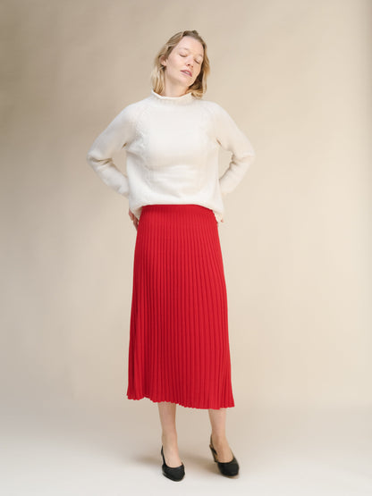 Full-length view of a modelo con a cream knit sweater with a red falda midi acanalada and black heels.