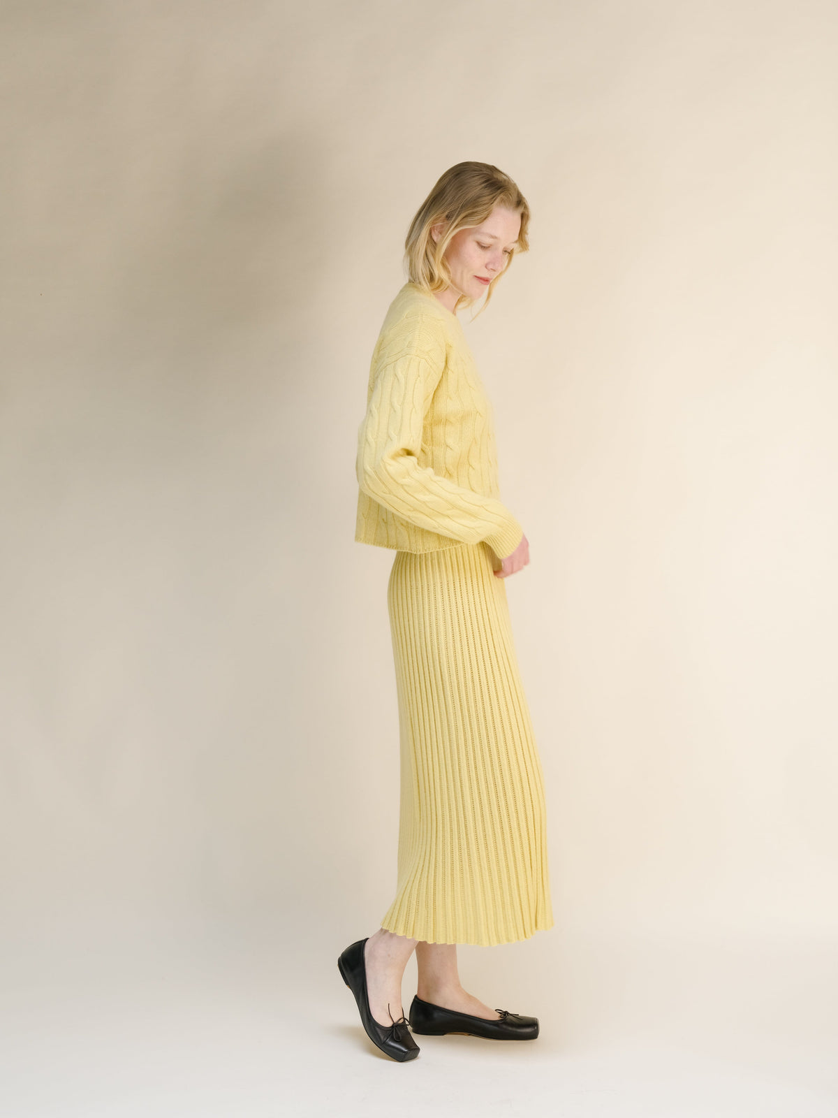 Vista lateral of a mujer con a amarillo pálido cashmere blend knit skirt with a jersey a juego against a neutral backdrop.