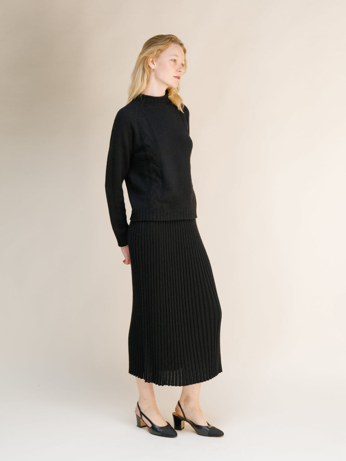 Vista lateral of a model in a black falda calada de mezcla de cachemira en punto 3D combinada con a coordinating knit sweater