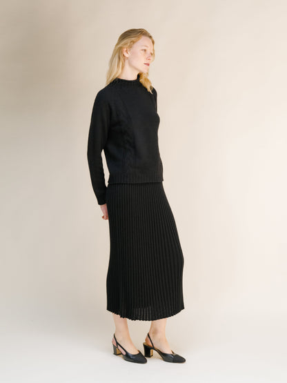 Vista lateral of a model in a black falda calada de mezcla de cachemira en punto 3D combinada con a coordinating knit sweater