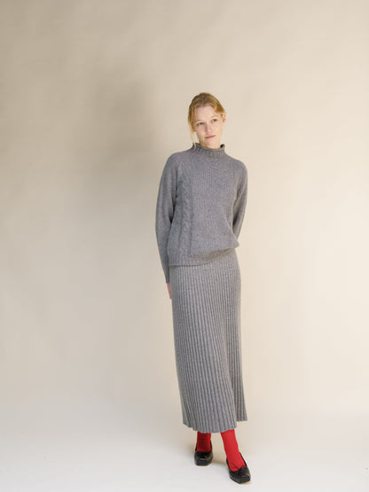 Full-length shot of a woman in a gray jersey de punto trenzado and matching falda maxi acanalada against a beige backdrop.