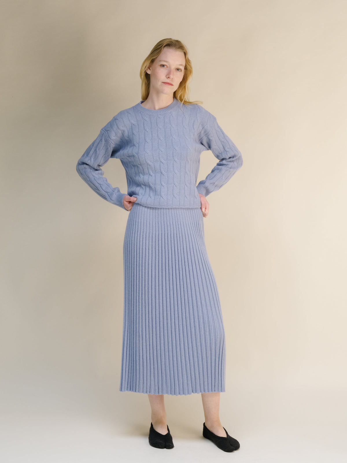 Modelo con azul pálido cashmere blend knit set scueroding with hands on hips against beige backdrop.