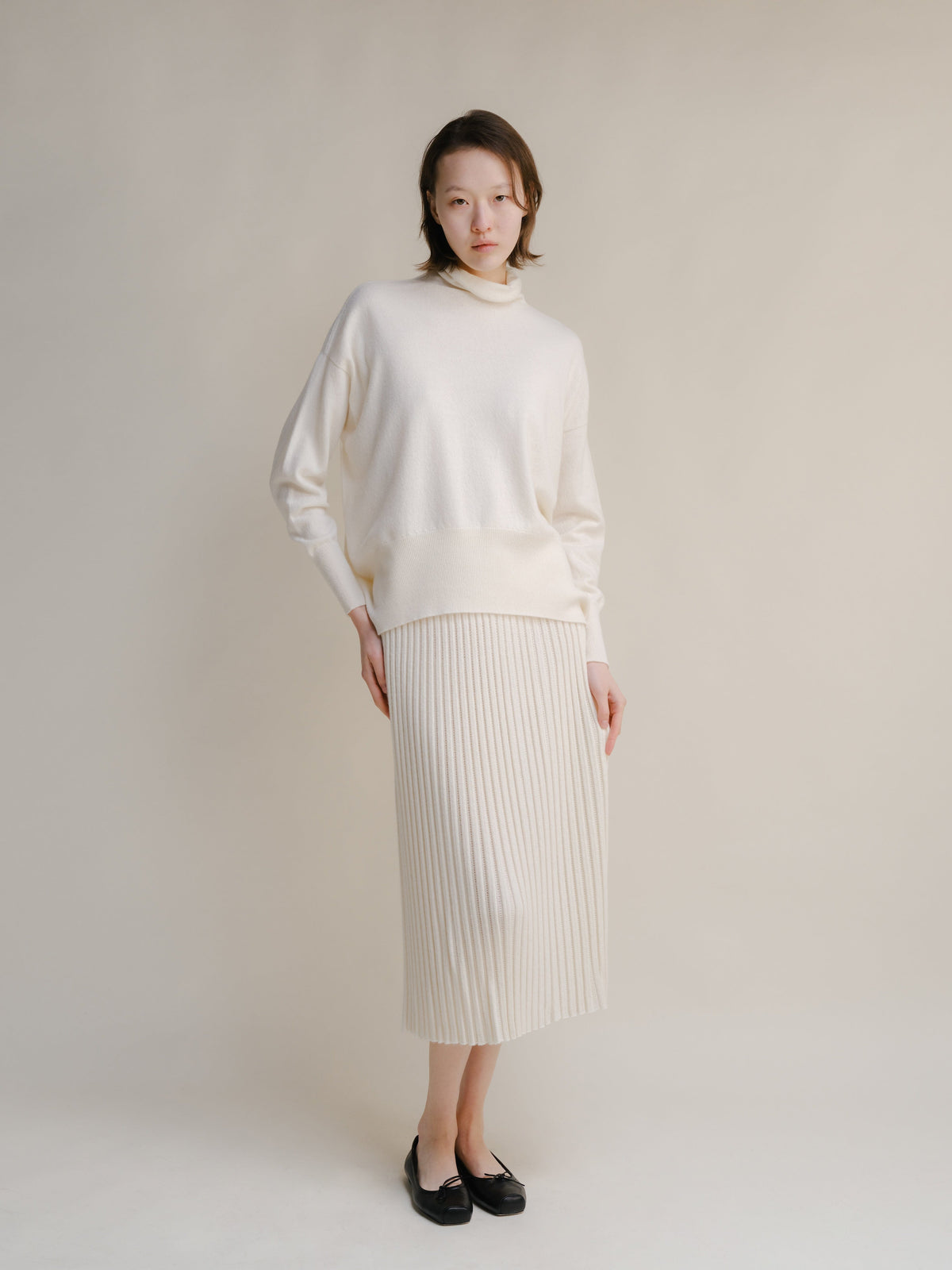 Crema jersey de cuello alto knit sweater with a falda midi acanalada a juego.