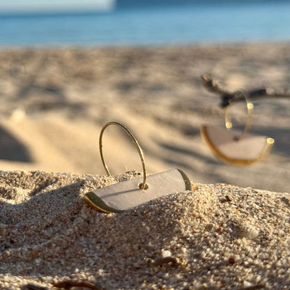 Doraluna white ceramic dangle earrings with gold luster resting in beach sand