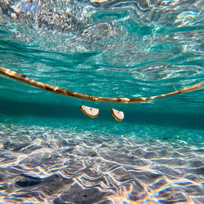 Ceramic earrings with gilded edges floating in clear blue water with a sandy ocean floor.