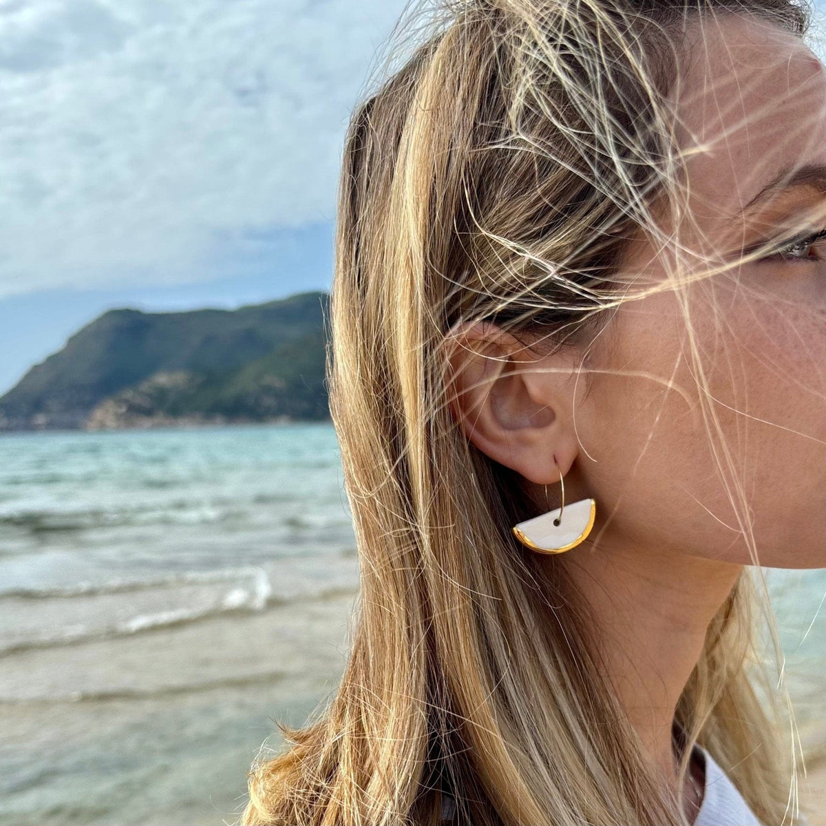 White ceramic crescent dangle earrings with gold edges on a slim hoop ear wire