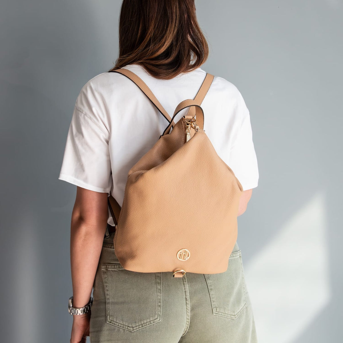Back view of a person wearing the Dublin cuoio leather backpack con shoulder straps over a bianco t-shirt e olive pants.
