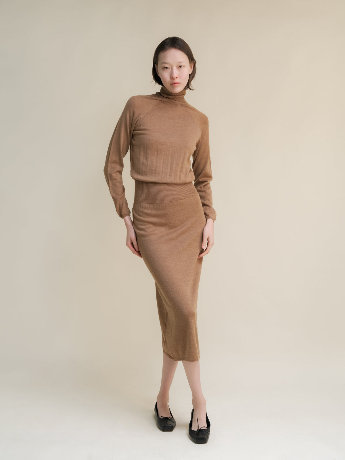 Model wearing camel brown knit turtleneck top with a matching midi skirt.