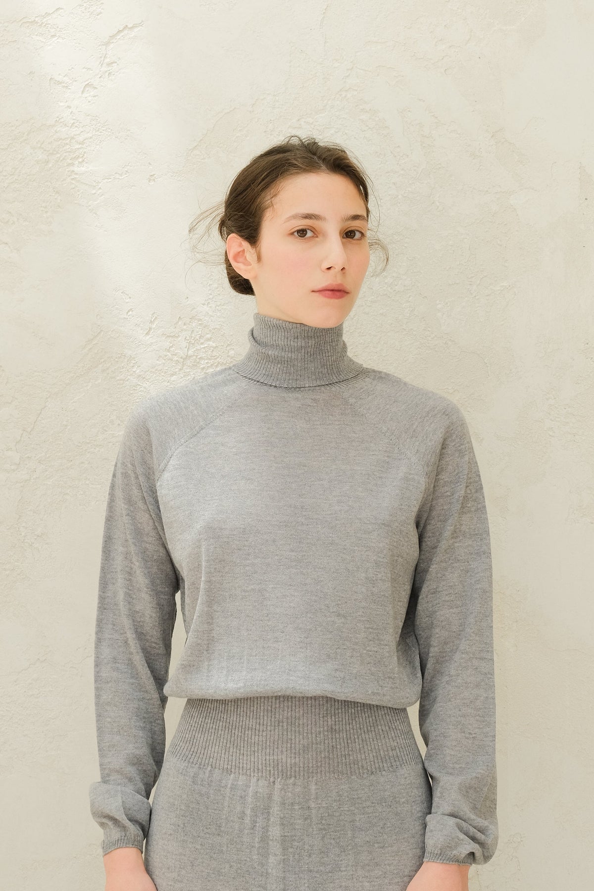 Close up of light grey knit turtleneck top with ribbed waistband and cuffs from the 3D-Knit Merino Wool set.