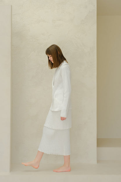 Side profile of a model in a white blazer de punto with a layered falda larga plisada from Fine Cotton Plissé