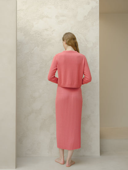 Back view of coral knit cropped cardigan with a matching long falda plisada worn by a barefoot model.