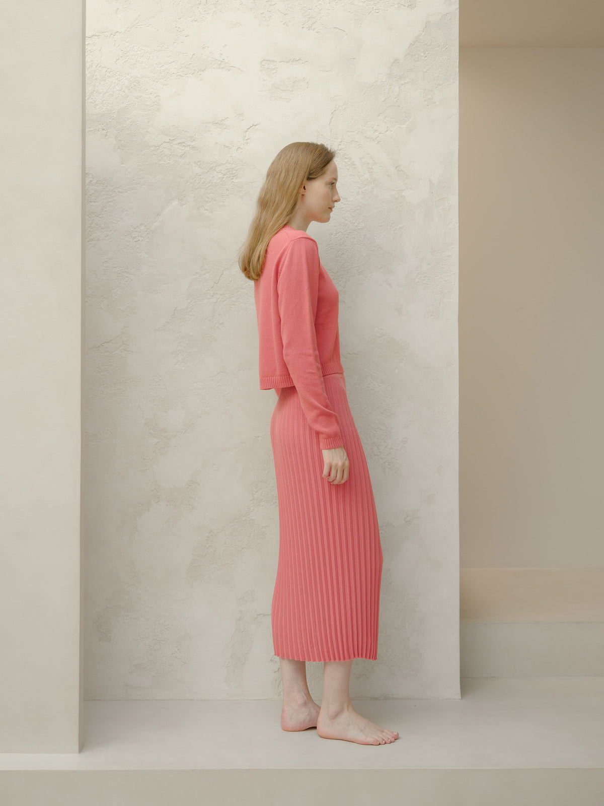 Vista lateral of a model in a rosa empolvado 3D Knit falda larga plisada de algodón fino with a cropped jersey a juego.