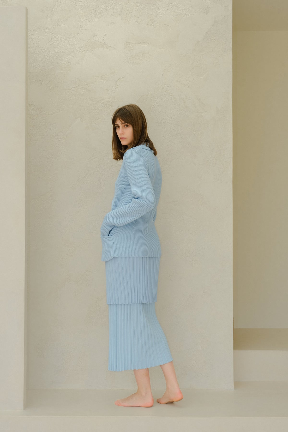 Vista lateral of a modelo con a azul claro falda larga plisada de algodón fino with a matching knit sweater in a neutral studio setting.