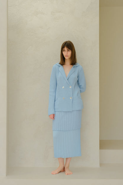 Vista frontal of a model in azul pálido ribbed knit double-breasted jacket with a layered falda plisada.