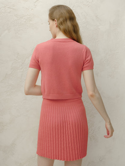 Back view of a modelo con a coral pink knitted top and matching pleated minifalda