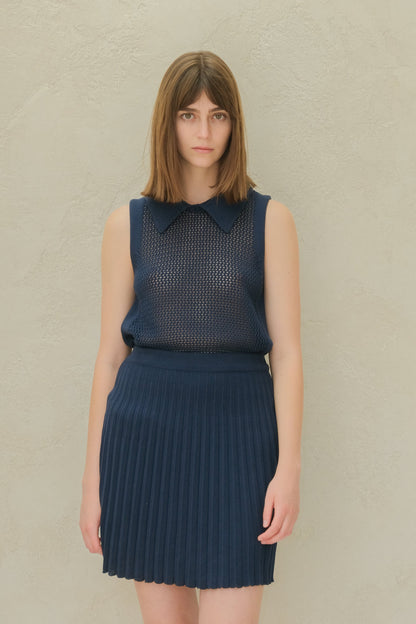 Azul marino top de punto sin mangas with a mesh pattern and a cuello puntiagudo, combinada con a azul marino pleated minifalda.
