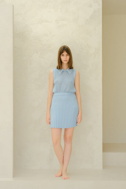 Mujer con a azul claro sleeveless top and skirt against a neutral background