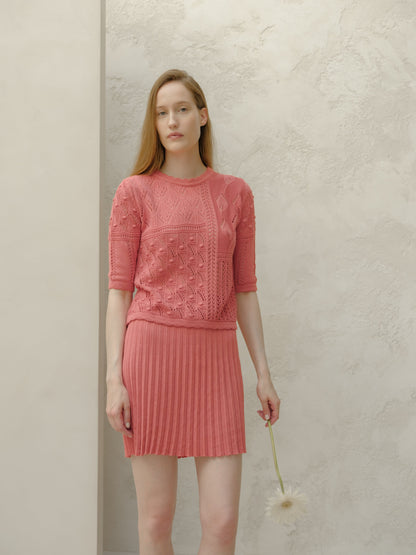 Vista frontal of a model in a pink minifalda plisada de algodón fino and top de punto a juego against a light textured wall.