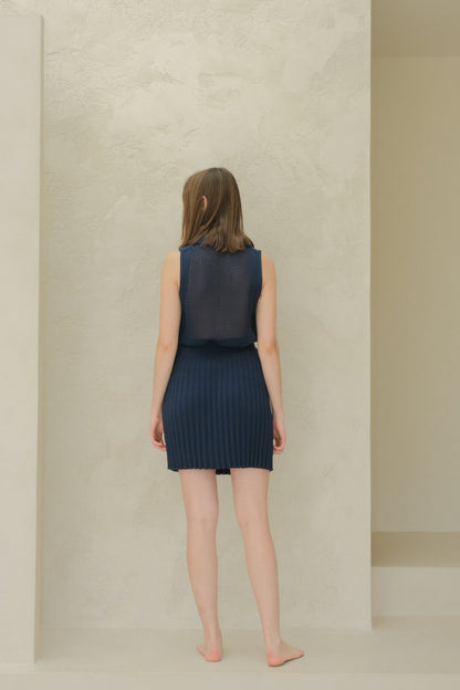 Back view of a model in a azul marino sleeveless top de punto calado with a cuello puntiagudo and pleated minifalda.