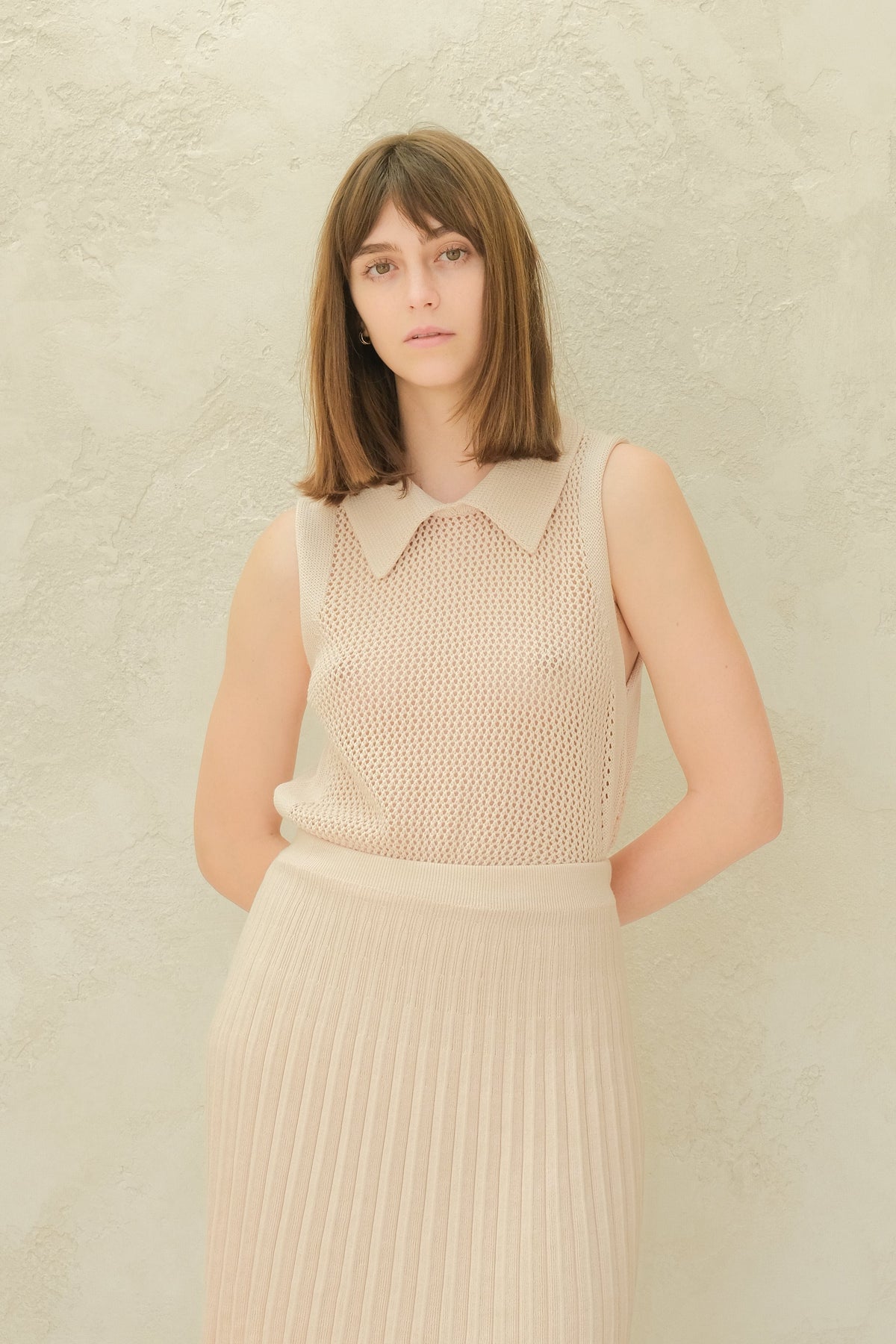 Modelo con cream top de punto sin mangas with a cuello puntiagudo and a matching pleated minifalda.