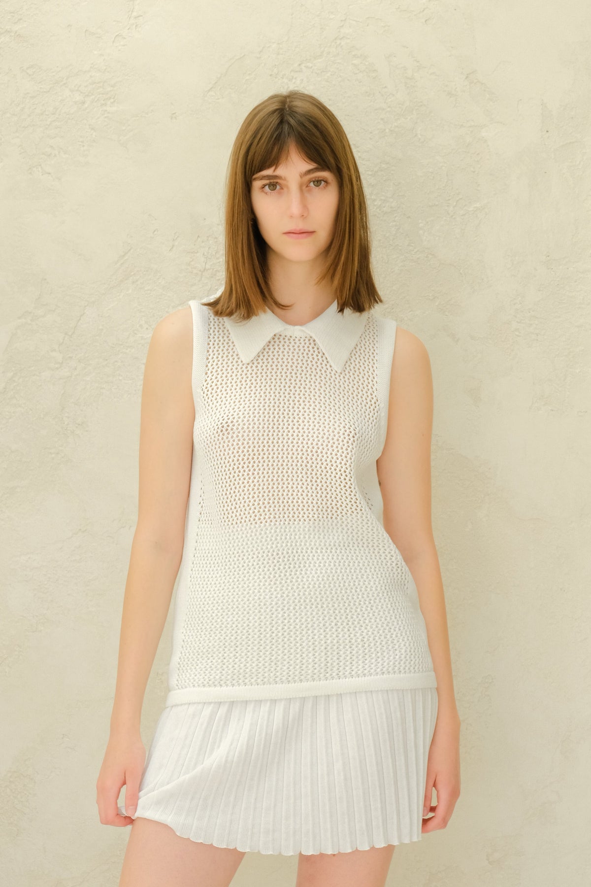 Modelo con a white mesh sleeveless top with a collared neckline and a white plissé minifalda.
