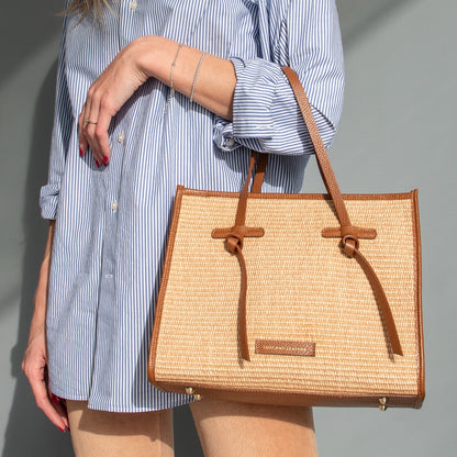 Model holds a reccognacfarbengular straw effect bag with brown leather trim and handles.
