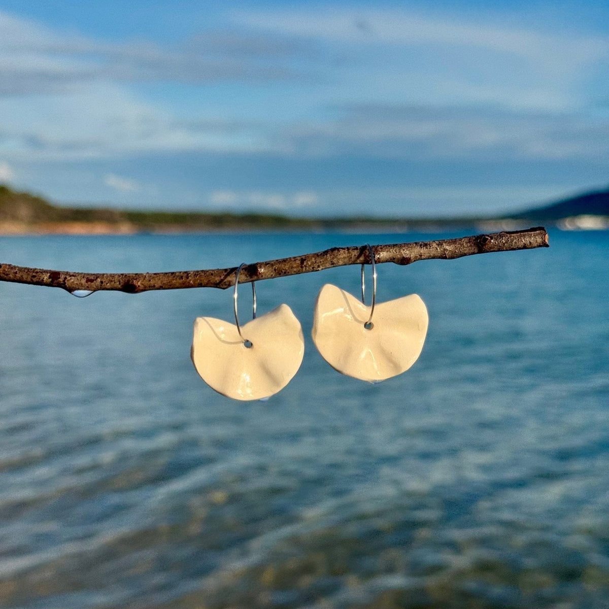 Pendientes colgantes Frolla de cerámica blanca suspendidos de una rama sobre el mar azul