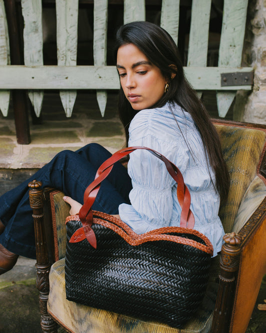 Léafa - Hewoven Leather Shoulder Bag | Marrone & Nero showcasing a woven nero leather body con marrone leather heles resting on a chair.