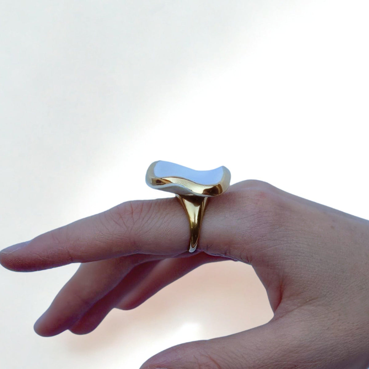 Goldfarbener Ring mit glänzendem unregelmäßigem weißem Keramikelement am Finger