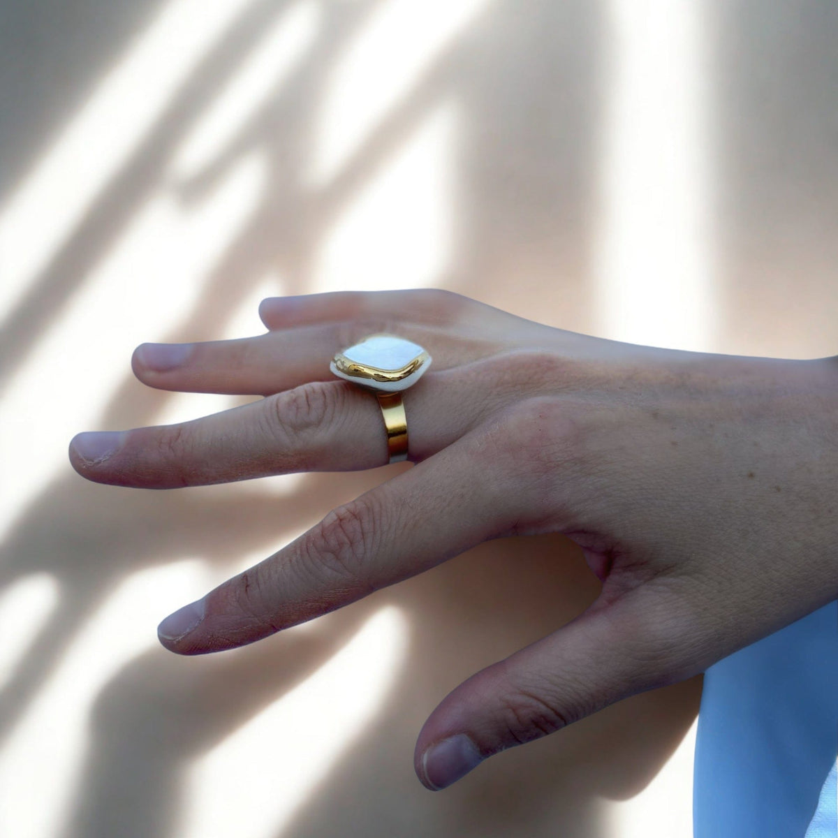 Seitenansicht of a gold ring with a white ceramic top on a finger